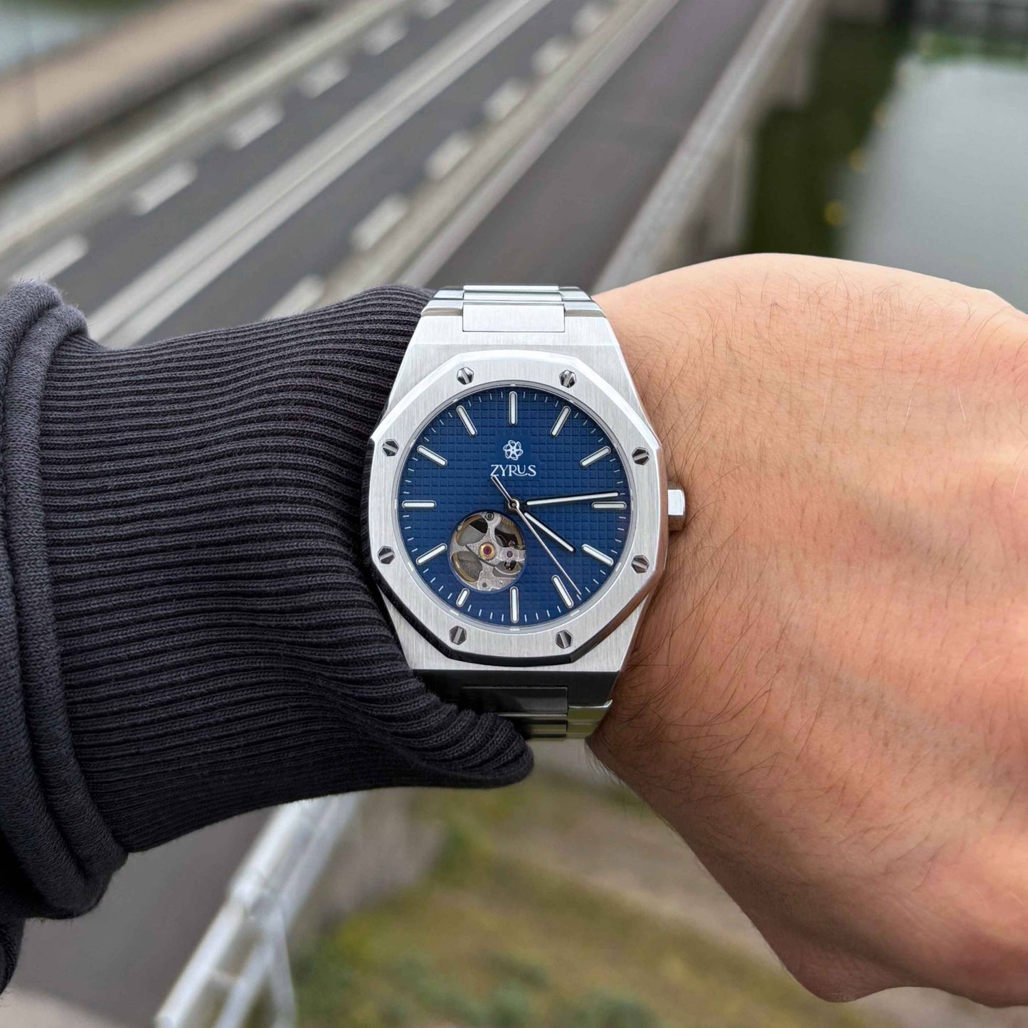 Zyrus Open Heart Watch in silver with a blue dial, worn in a lifestyle setting, highlighting its sophisticated design and craftsmanship.