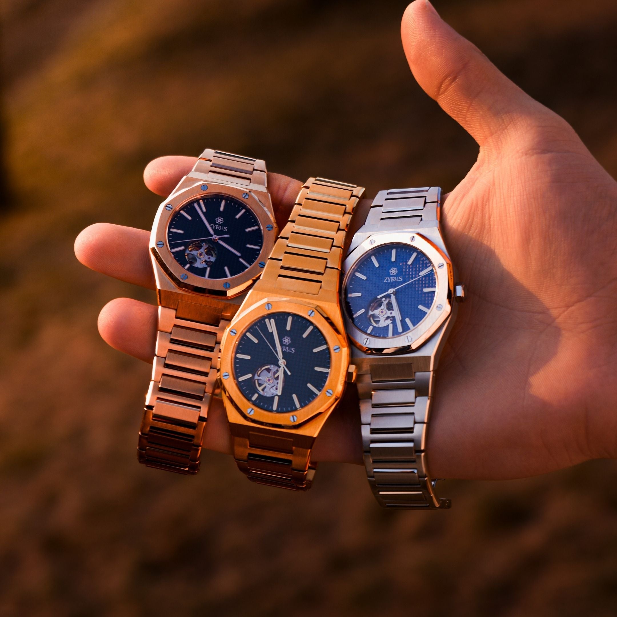 Zyrus Open Heart Watches in silver, gold, and rose gold, beautifully displayed against a sunset backdrop, highlighting luxury and elegance.